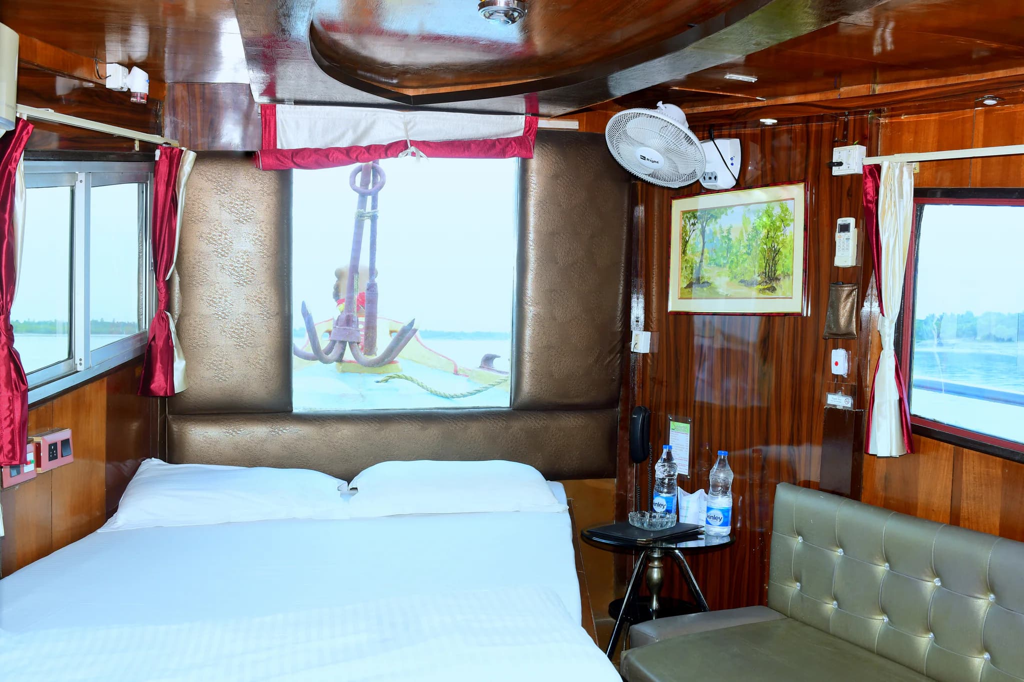 Cabin aboard Whispering Winds with a bed, river-facing windows and seating